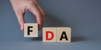 A hand holding a wooden block with the letter F, next to blocks spelling FDA