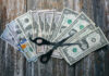 Patriotic Price Cut — Or Power Play? Scissors placed on a spread of various U.S. dollar bills