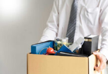 100,000 Jobs Bombshell – 50,000 Already Gone Person holding a box of personal office items.
