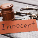 A wooden gavel next to handcuffs and a card that says 'Innocent'