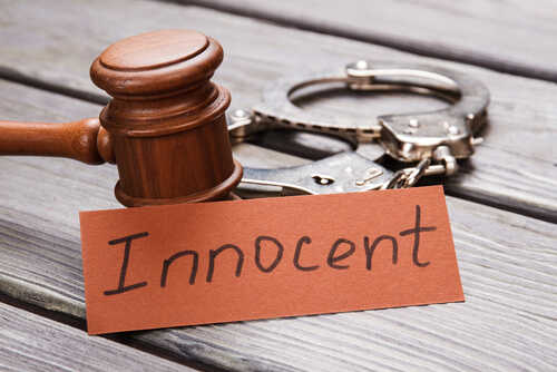 A wooden gavel next to handcuffs and a card that says 'Innocent'