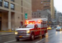 Rescuers Tunnel 100 Hours — Then This! Ambulance with flashing lights driving on a wet city street
