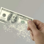 Hand holding a disintegrating hundred dollar bill.