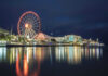 Ferris wheel and waterfront lights reflecting on water.