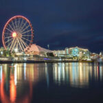 Ferris wheel and waterfront lights reflecting on water.