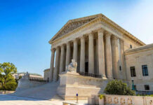 Stone building with columns and statues, clear blue sky.