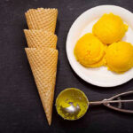 Ice cream scoops, cones, and scoop tool on black background.