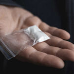 Hand holding small bag of white powder.