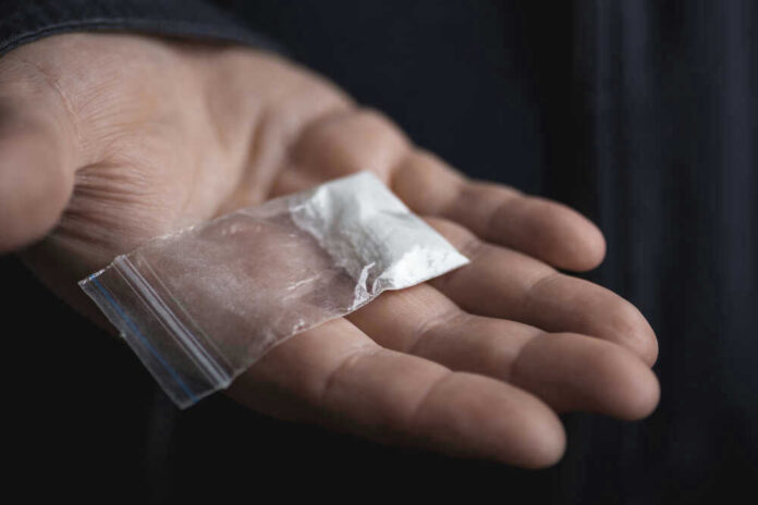 Hand holding small bag of white powder.