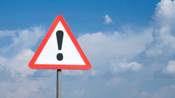 Triangle warning sign with exclamation mark against sky.