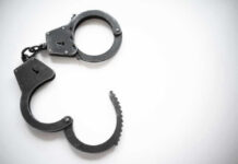 Convicted Killer Nabbed In Horrific Firestorm Open metal handcuffs on white background.
