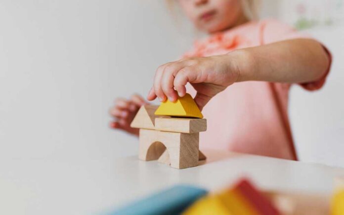 Little,Child,Girl,Playing,Wooden,Building,Blocks,At,Home,Or Sad child sitting against brick wall, kids running away.