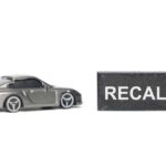 Biggest Tesla Recall — Not Just Tesla A miniature gray sports car next to a black sign that reads 'RECALL'