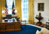 Presidential office with desk, flags, and portraits.