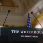 Sudden Podium Exit Stuns West Wing Press podium with the White House sign and an American flag in the background