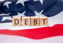 Wooden blocks spelling 'DEBT' on an American flag background