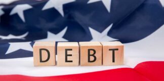 Wooden blocks spelling 'DEBT' on an American flag background