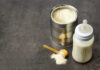 A can of powdered baby formula next to a feeding bottle with milk