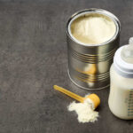 A can of powdered baby formula next to a feeding bottle with milk