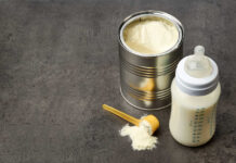 A can of powdered baby formula next to a feeding bottle with milk