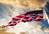 American flag waving against a cloudy sky.