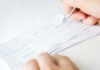 As THESE Costs SURGE Paychecks Get Squeezed Person signing a check on a white background.