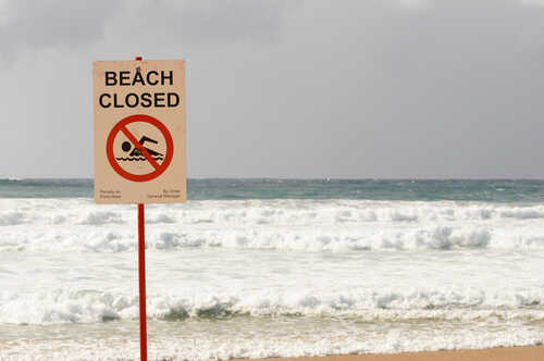 "beach,Closed",Sign,With,Choppy,Seas,In,The,Background,At Sign indicating the beach is closed with a no swimming symbol