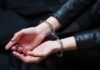 Hands in handcuffs resting on a dark surface