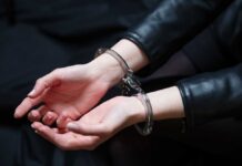 Cold-Case Murder: Mom Arrested! Hands in handcuffs resting on a dark surface
