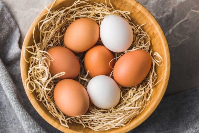 Brown and white eggs in a wooden bowl with straw