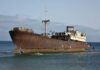 Unmasked 1884 Ghost Ship Shocks U.S. An abandoned, rusted ship stranded on the shore with a calm ocean in the background