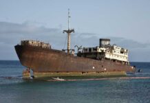 An abandoned, rusted ship stranded on the shore with a calm ocean in the background