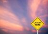 Yellow diamond sign reading latest news against a colorful sunset sky