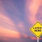 Yellow diamond sign reading latest news against a colorful sunset sky