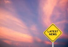 Yellow diamond sign reading latest news against a colorful sunset sky