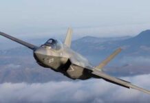 F-35 fighter jet flying above clouds with mountains in the background