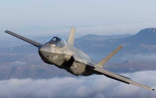 F-35 fighter jet flying above clouds with mountains in the background