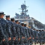 Navy personnel marching in formation towards a ship