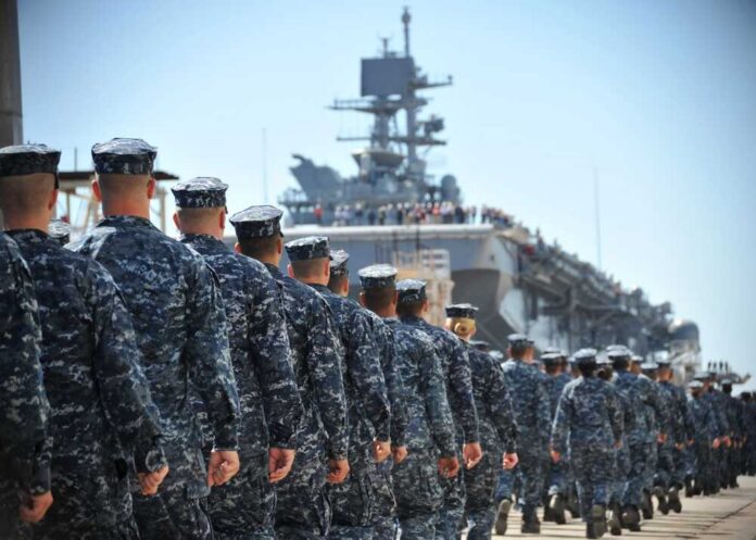 U.s.,Sailors,And,Marines,Assigned,To,The,Amphibious,Assault,Ship Navy personnel marching in formation towards a ship