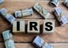 Wooden blocks spelling IRS surrounded by rolled currency notes