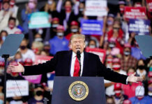 Donald Trump speaking at a rally with arms outstretched