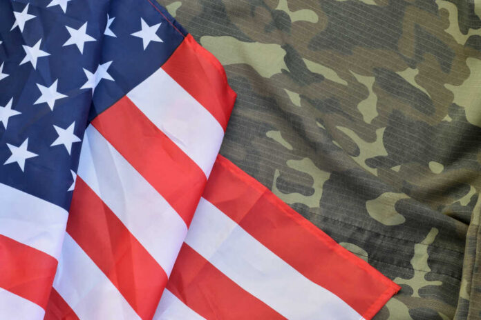 United,States,Of,America,Flag,And,Folded,Military,Uniform,Jacket. American flag draped over camouflage fabric