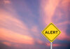 Yellow alert sign against a colorful sunset sky