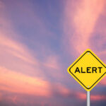 Yellow alert sign against a colorful sunset sky
