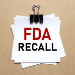 A notice labeled 'FDA RECALL' clipped to white papers on a brown background