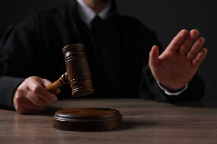 shutterstock_2381854215 Judge holding gavel, hand raised in courtroom.