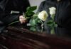Two individuals placing white roses on a coffin during a funeral
