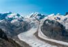 Alps Hit Hard – Glaciers Suddenly Shrink Glacier winding through snow-capped alpine mountains under a clear blue sky