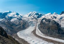 Glacier winding through snow-capped alpine mountains under a clear blue sky