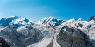Glacier winding through snow-capped alpine mountains under a clear blue sky